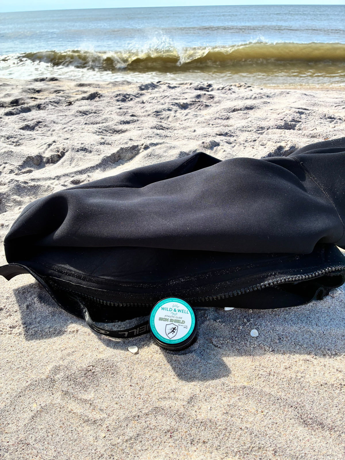 Skin Shield athletic glide balm on the beach beside a wetsuit 